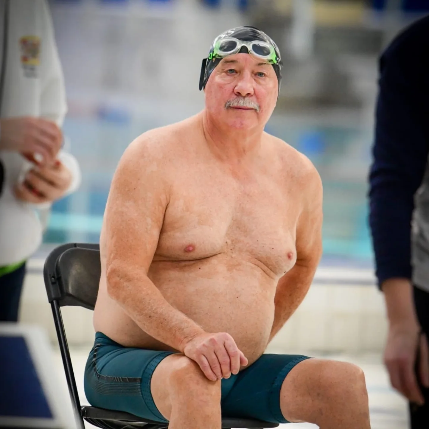 A club veteran in cap and goggles waiting poolside between races