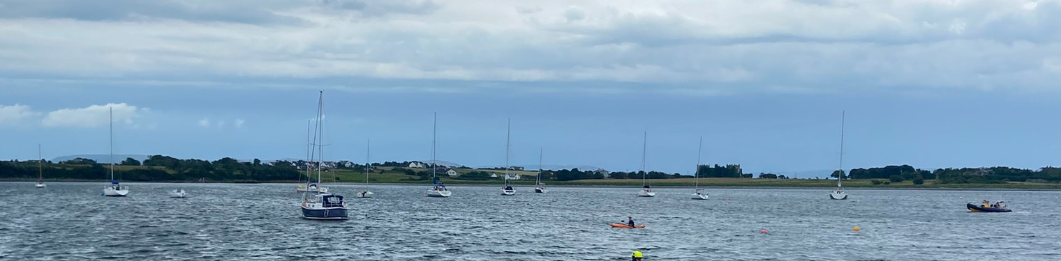 Open water off the Irish coast — sailing boats at anchor, a kayak escort and a lone swimmer